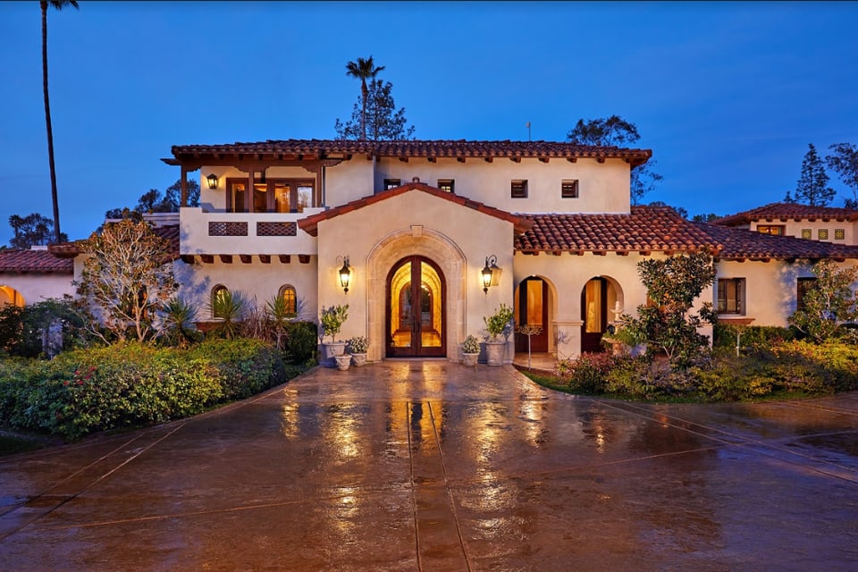 Covenant Builders Lago Lindo Spanish-style estate in Rancho Santa Fe, with a warmly lit arched entrance at twilight
